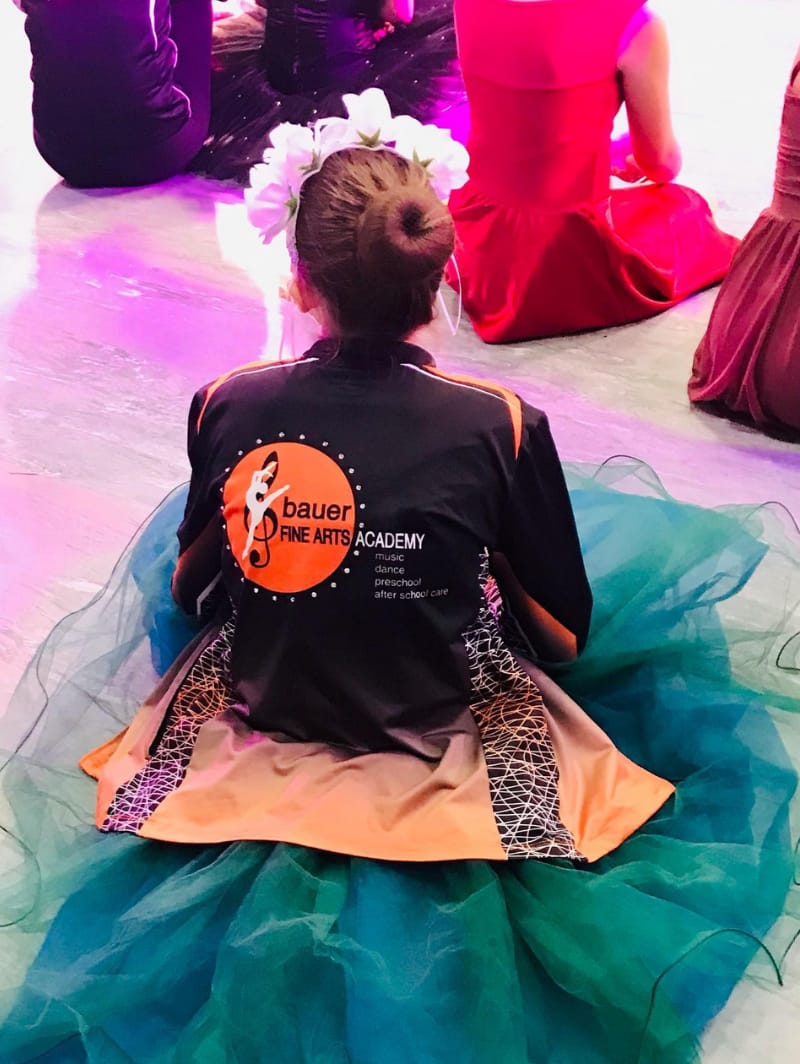 Young girl wearing a Bauer Fine Arts Academy jacket while sitting on stage