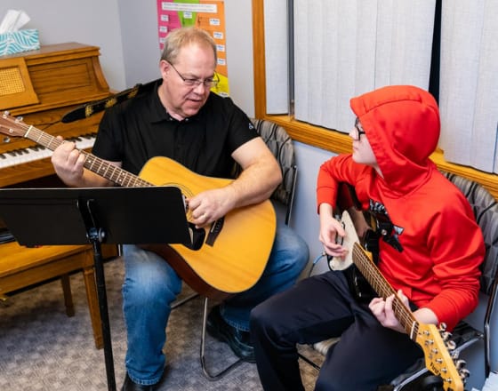 Music teacher showing a boy how to play guitar at Bauer Fine Arts Academy