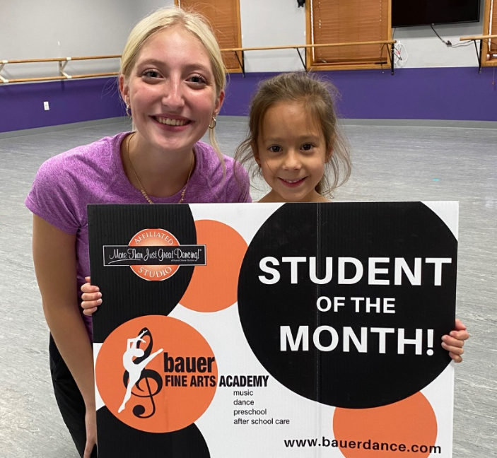 Girl holding a "Student of the Month" sign with a Bauer Fine Arts Academy instructor